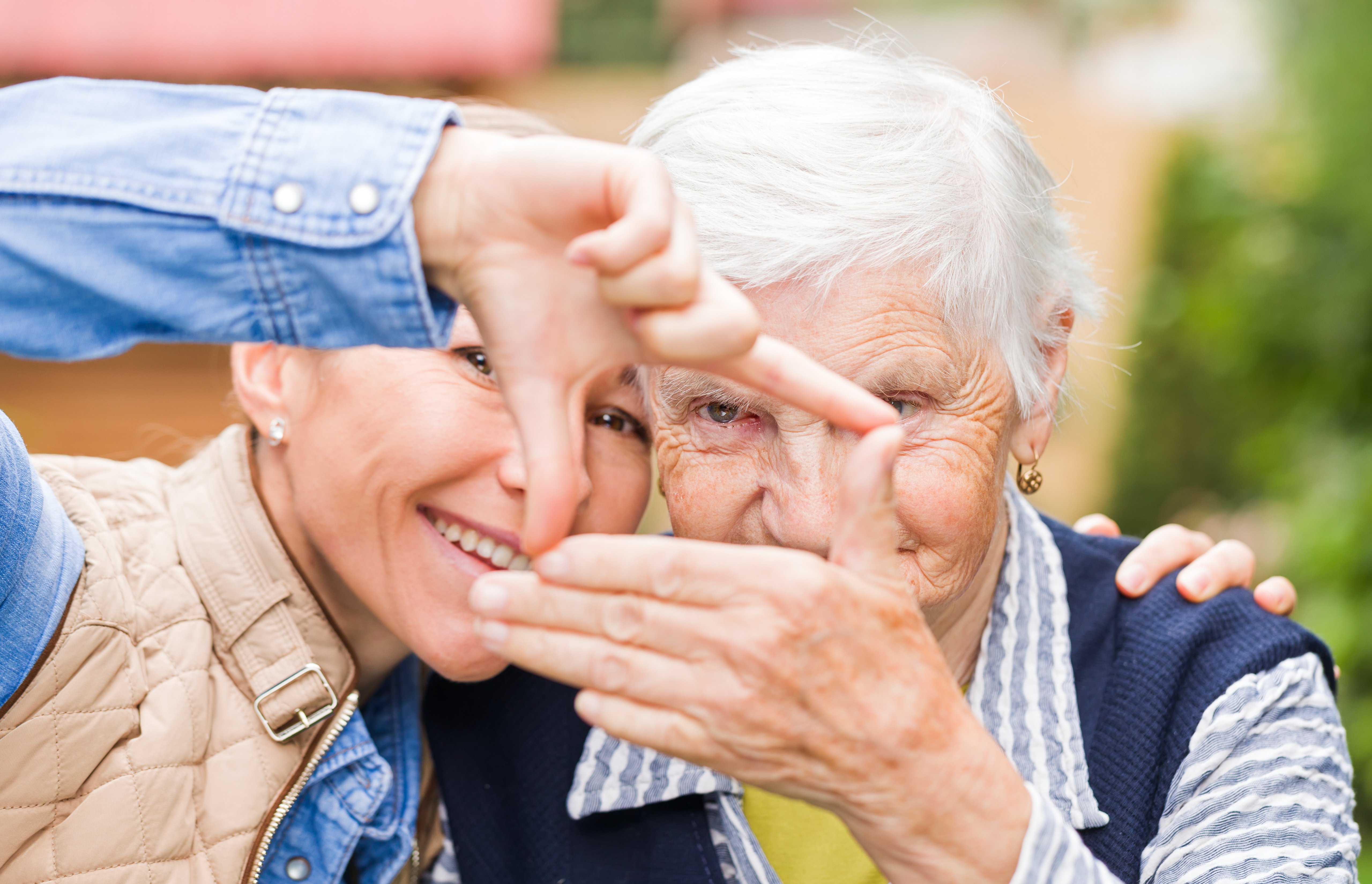 Two older adults sit side by side making a window with their hands. 